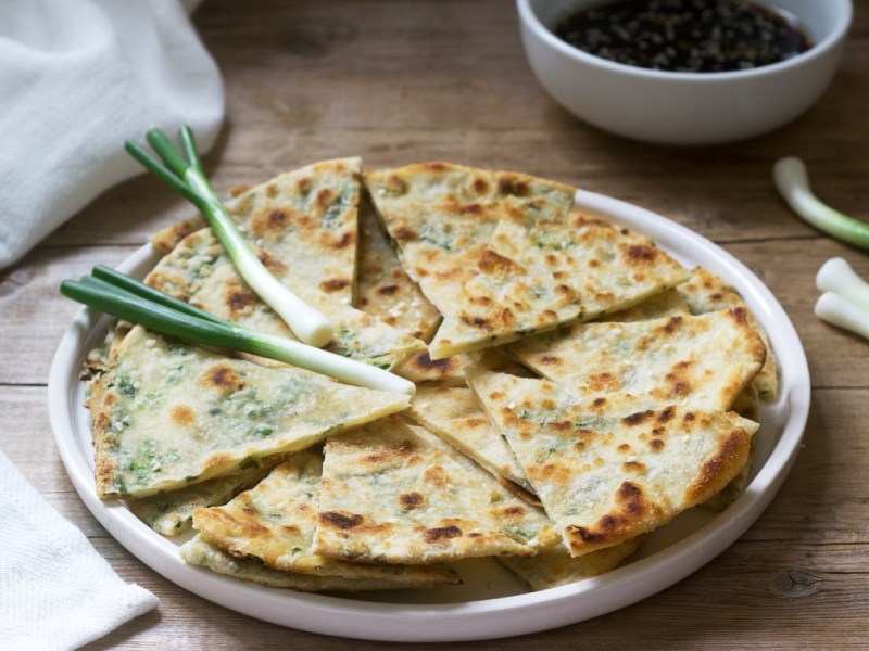 Mehrere in Stücke geschnittene Pfannkuchen mit Frühlingszwiebeln auf einem Teller. Obendrauf liegen ein paar Lauchzwiebeln.