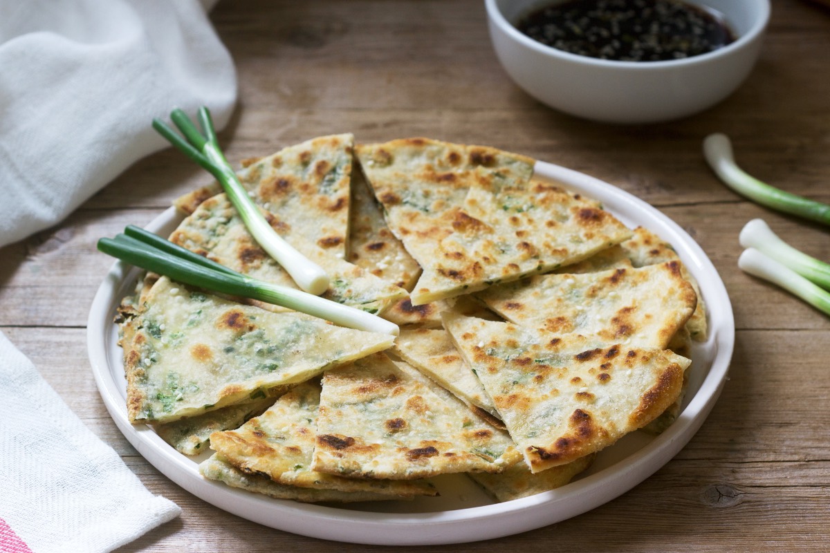 Mehrere in Stücke geschnittene Pfannkuchen mit Frühlingszwiebeln auf einem Teller. Obendrauf liegen ein paar Lauchzwiebeln.