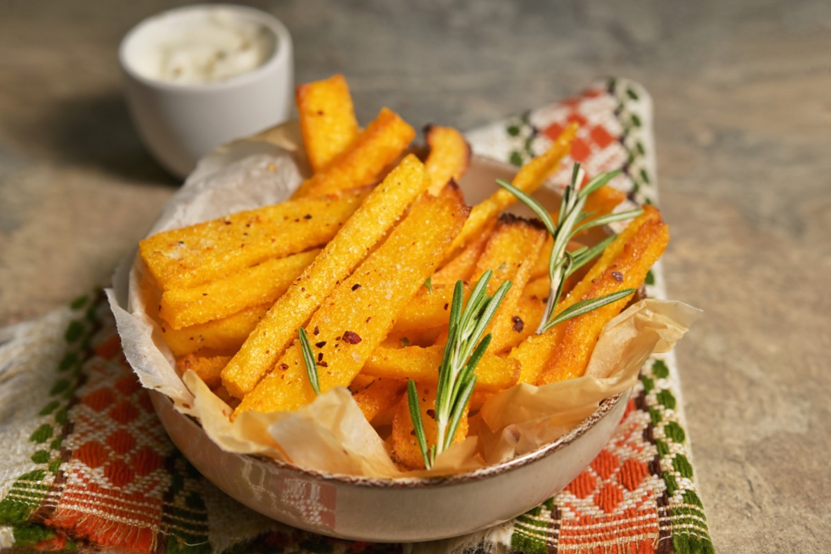 Polenta-Pommes in einer Schüssel. Daneben steht ein Schälchen mit Dip.