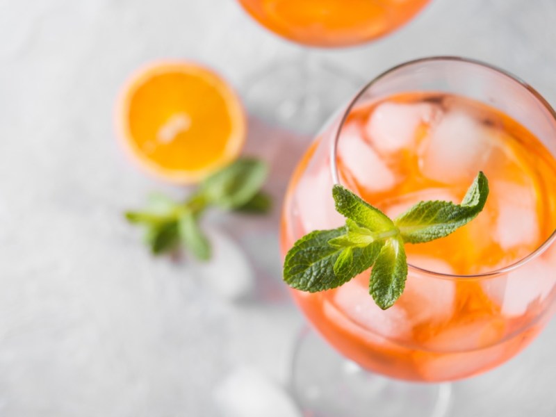 Ein Glas Rhabarber Spritz mit Minze von oben fotografiert. Daneben liegen eine Orangenscheibe und Minzblätter.