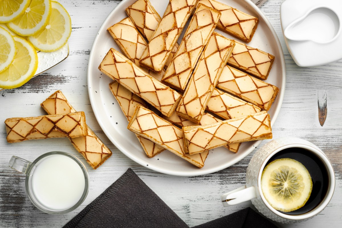 Sfogliatine, italienische Blätterteigkekse, auf einem weißen Teller. Daneben eine Tasse und eine Kanne Milch, einige Zitronenscheiben und ein Tee mit Zitrone.