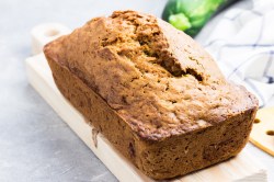 Süßes Zucchinibrot auf einem weißen Brett, im Hintergrund eine Zucchini.