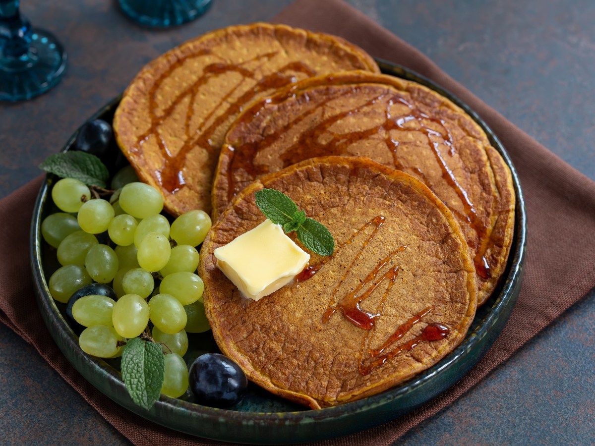 Süßkartoffel-Pancakes mit Butter und Weitrauben auf dunklem Teller