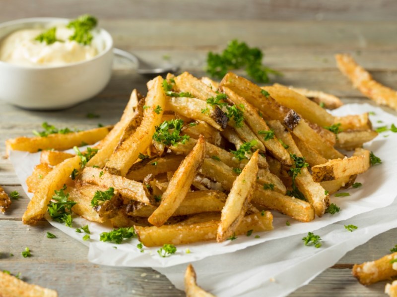 Eine Portion Trüffelpommes mit Petersilie und einer Schale mit Dip.