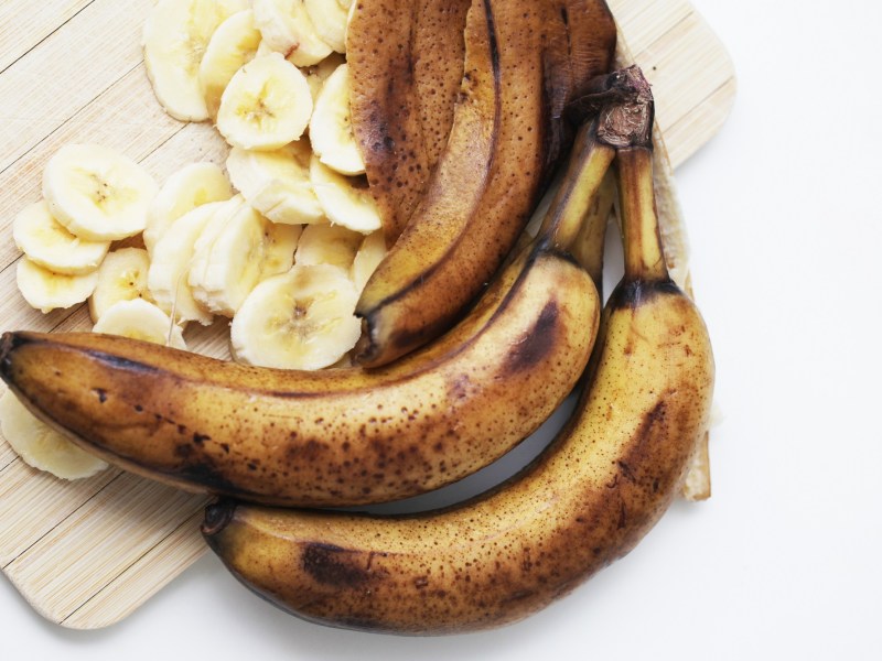 Versteckter Alkohol in Lebensmitteln: zwei überreife Bananen auf einem Holzbrett, daneben weitere Bananenschalen und Bananenscheiben.
