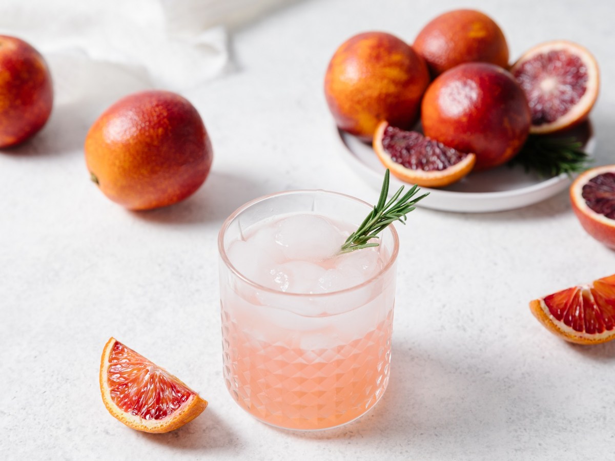 Ein Glas Aperol Paloma mit Eiswürfeln und Grapefruits daneben.