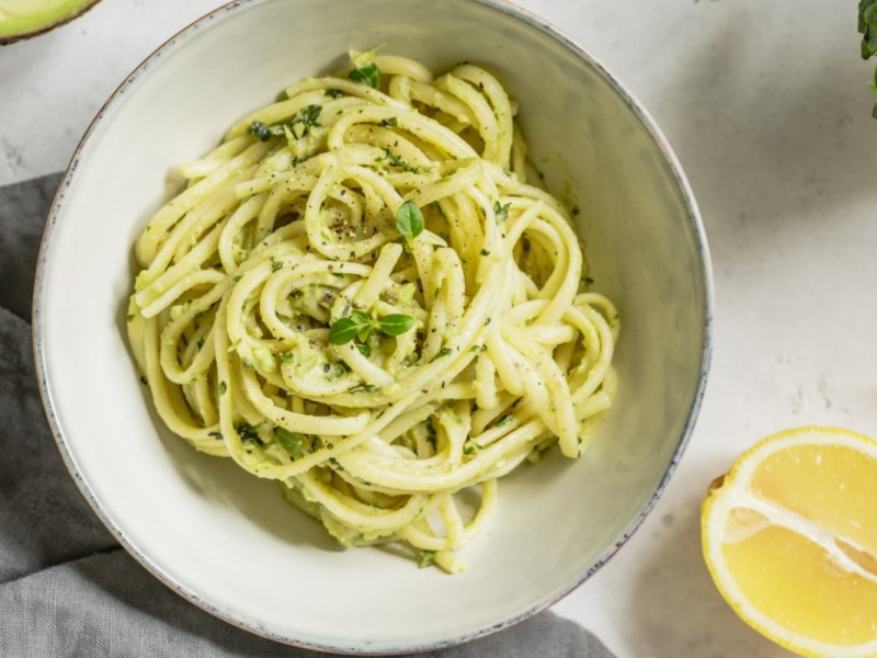 Ein Teller Avocado-Basilikum-Pasta in der Draufsicht. Drumherum liegen frische Zutaten.