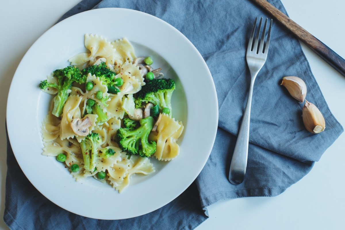 Ein Teller mit Brokkoli-Champignon-Pasta mit Erbsen. Daneben liegt Besteck.