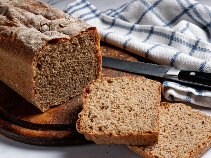 Brot backen ohne Hefe: ein angeschnittenes Kastenbrot, daneben ein kariertes Geschirrtuch.
