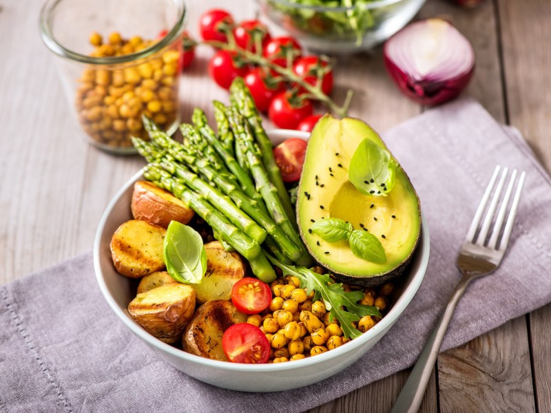 Schüssel mit Buddha Bowl mit Spargel, Gabe daneben.