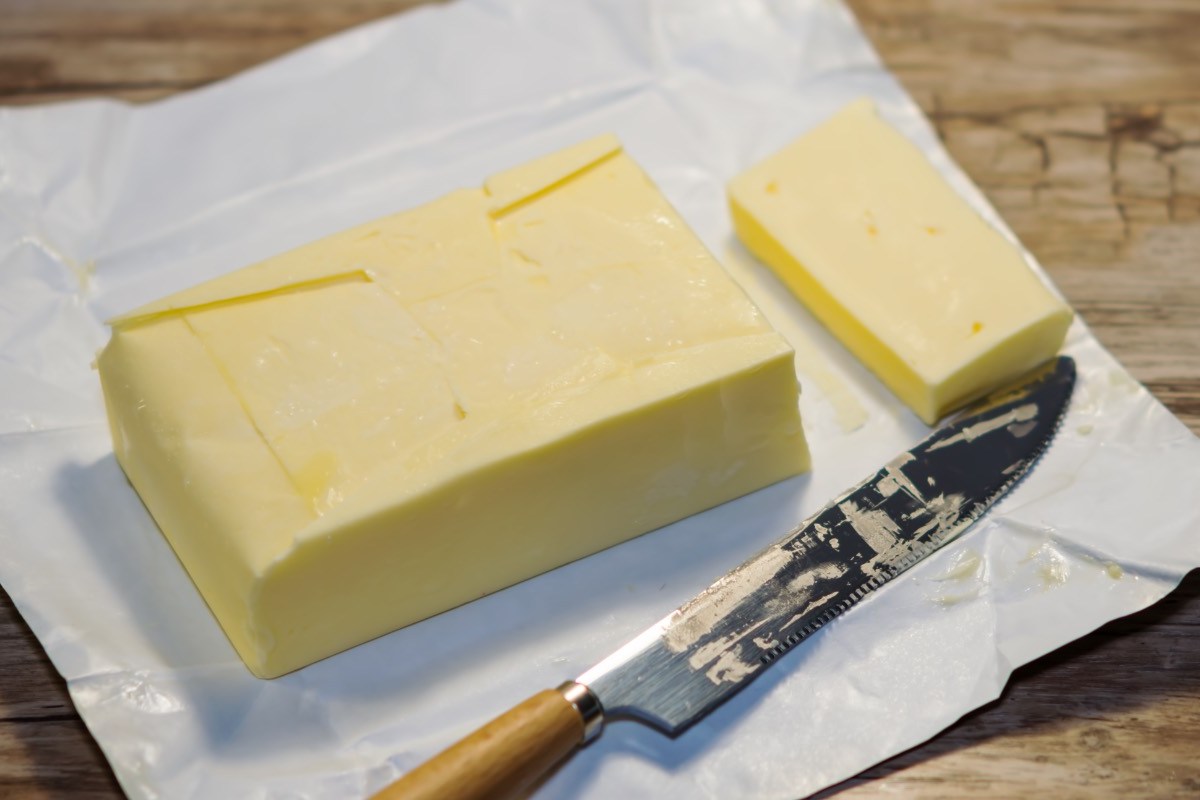 Ein Stück eingefrorene Butter, von dem mit einem Messer eine Scheibe abgeschnitten wurde.