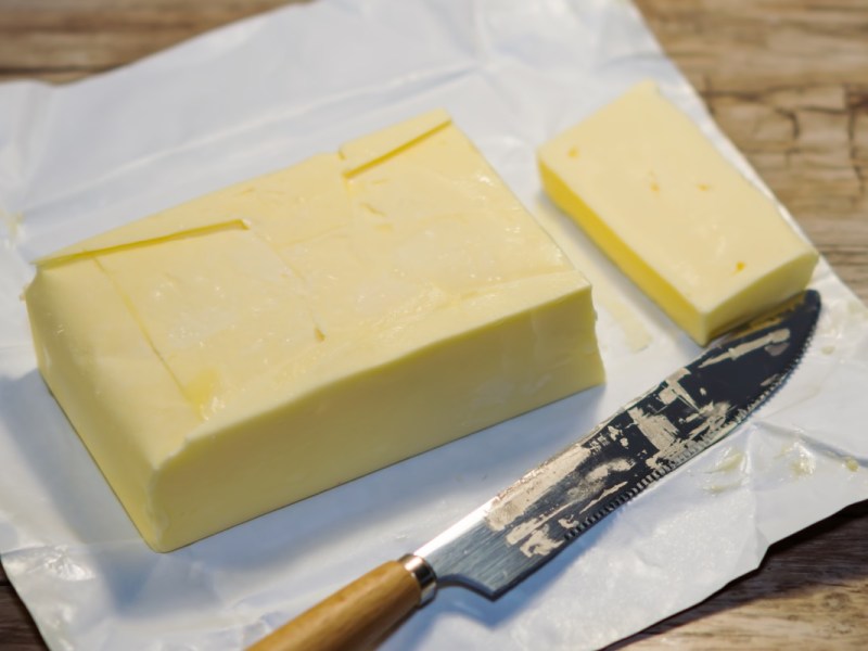 Ein Stück eingefrorene Butter, von dem mit einem Messer eine Scheibe abgeschnitten wurde.
