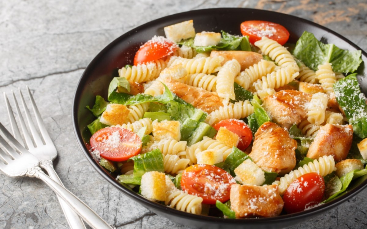 Ein Teller mit Caesar-Pasta-Salat, neben dem zwei Gabeln liegen.