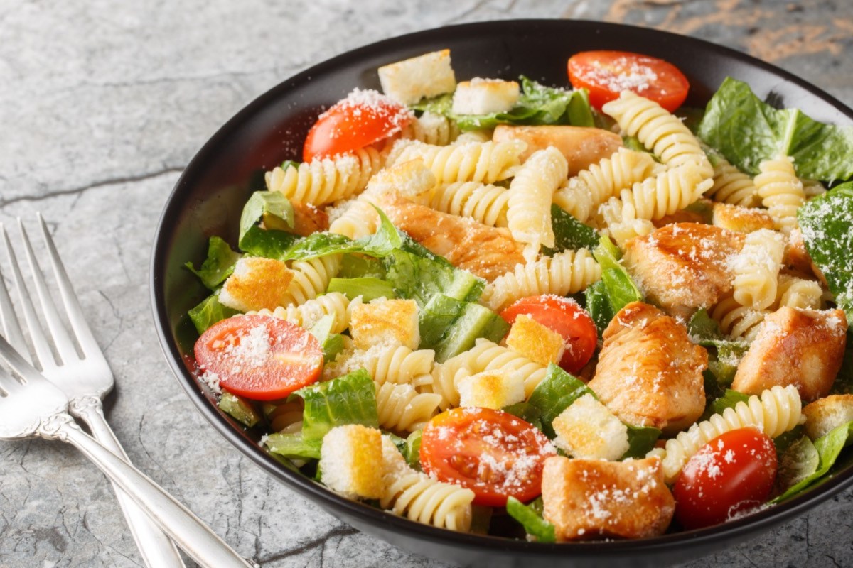 Ein Teller mit Caesar-Pasta-Salat, neben dem zwei Gabeln liegen.