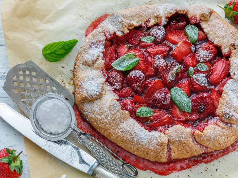 Eine mit Puderzucker und Basilikum dekorierte Erdbeer-Galette.