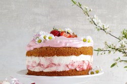 Erdbeer-Schmand-Torte mit zwei Kuchenböden und zwei Cremeschichten, garniert mit Erdbeeren, daneben blühende Zweige.