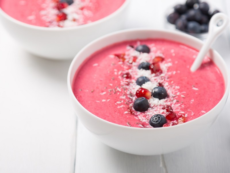 2 Erdbeer-Smoothie-Bowls garniert mit Blaubeeren, Kokosflocken und Granatapfelkernen.