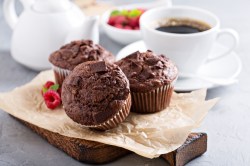 3 Espresso-Muffins mit Schokolade auf einem Brett, dahinter eine Tasse Kaffee.