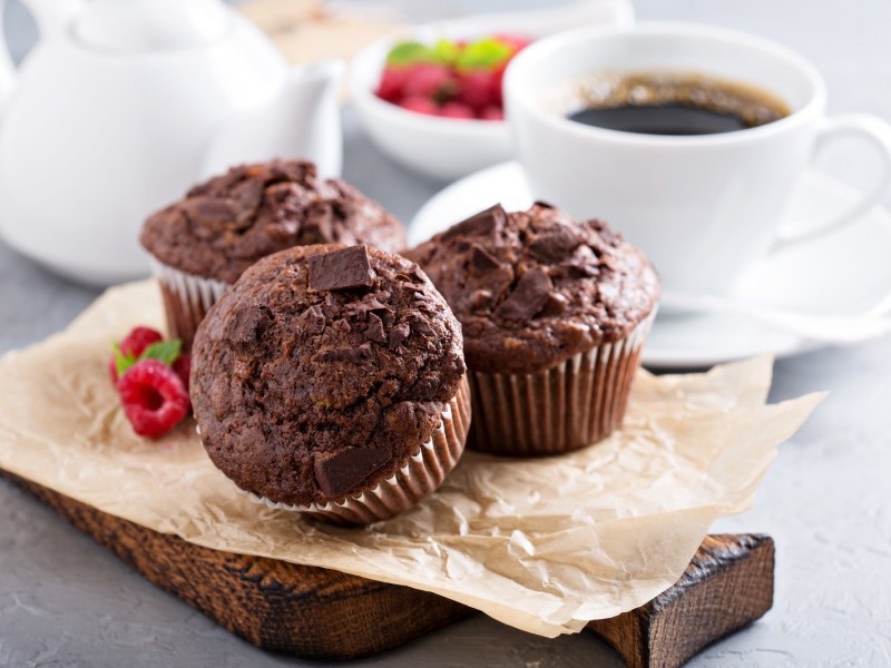 3 Espresso-Muffins mit Schokolade auf einem Brett, dahinter eine Tasse Kaffee.