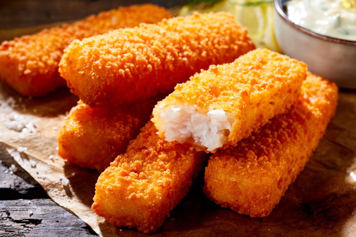 Einige selbst gemachte Fischstäbchen. Eine Schale mit Dip im Hintergrund.