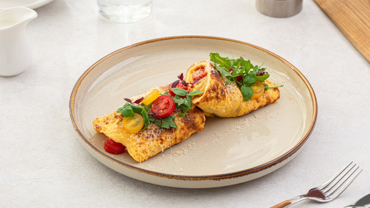 Französisches Käse-Omelett, garniert mit Kräutern und Tomaten auf einem weißen Teller.