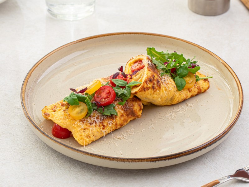 Französisches Käse-Omelett, garniert mit Kräutern und Tomaten auf einem weißen Teller.