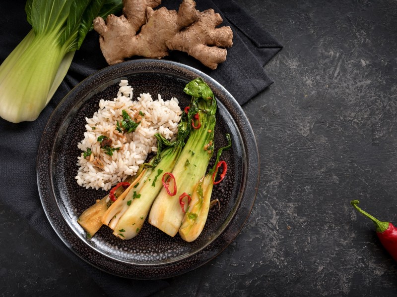 Teller mit gebratenem Pak Choi und Reis auf dunklem Untergrund