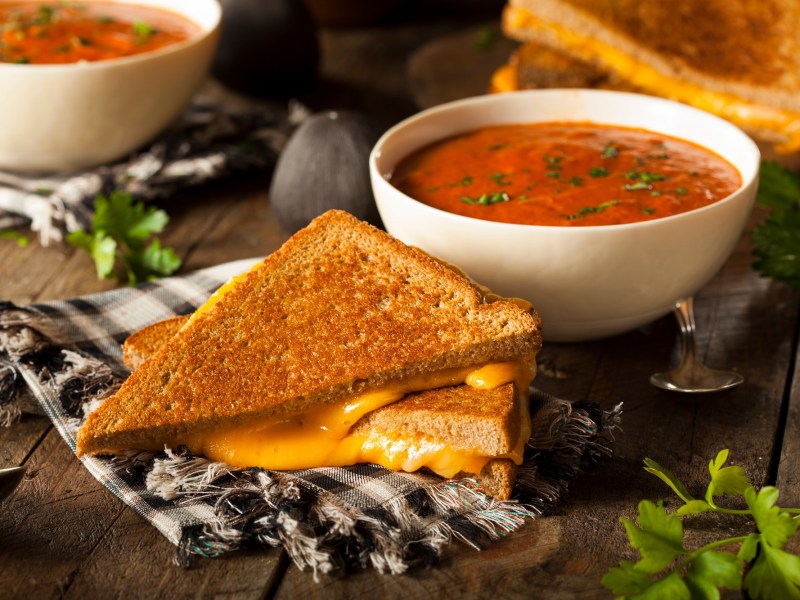 Grilled Cheese Sandwich mit Tomatensuppe auf einem Geschirrtuch angerichtet.