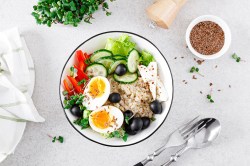 Eine Haferflocken-Bowl mit Feta und Ei, dazu Paprika, Salat, Gurken und Oliven.
