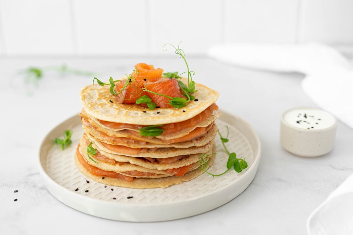 Teller mit Kräuter-Pancake mit Räucherlachs auf hellem Untergrund.