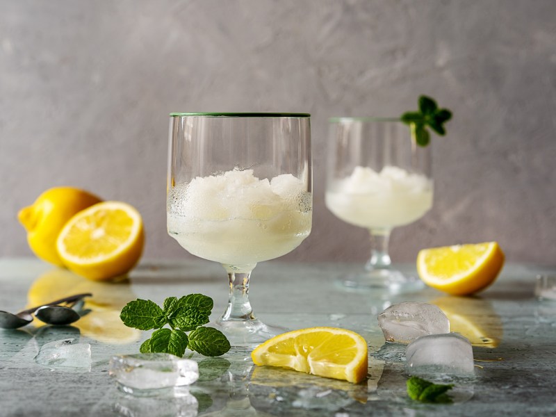 Original italienisches Zitronensorbet in zwei Gläsern, garniert mit Minze, daneben Zitronen.