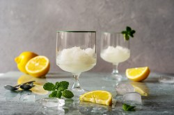Original italienisches Zitronensorbet in zwei Gläsern, garniert mit Minze, daneben Zitronen.