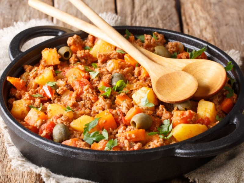 Picadillo, mexikanische Hackfleischpfanne, auf der zwei Holzlöffel liegen.