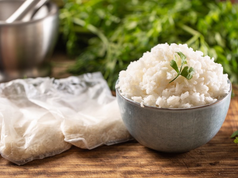 Reis einfrieren: eine Schüssel Reis, daneben Reisbeutel, im Hintergrund Kräuter.