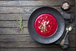 Rote-Bete-Apfel-Suppe, angerichtet auf einem dunkeln Teller auf einem Holztisch.