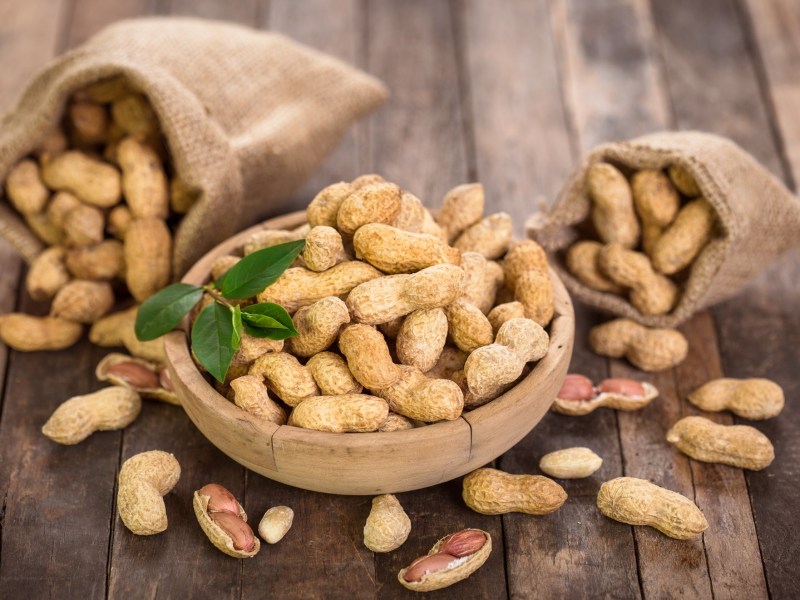 Sind Erdnüsse gesund: eine Schale mit Erdnüssen, daneben zwei kleine umgekippte Säcke mit Nüssen.
