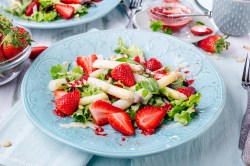 Spargel-Erdbeer-Salat auf einem hellblauen, gemusterten Teller. Im Hintergrund stehen mehr Teller mit Salat.