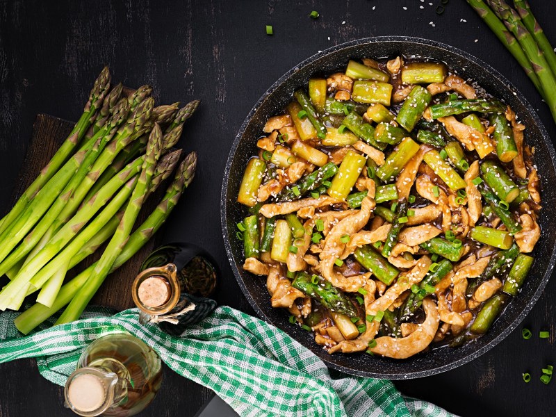 Spargel-Hähnchen-Pfanne, daneben liegen Stangen grüner Spargel und einige Flaschen mit Soja- und Austernsoße