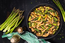 Spargel-Hähnchen-Pfanne, daneben liegen Stangen grüner Spargel und einige Flaschen mit Soja- und Austernsoße