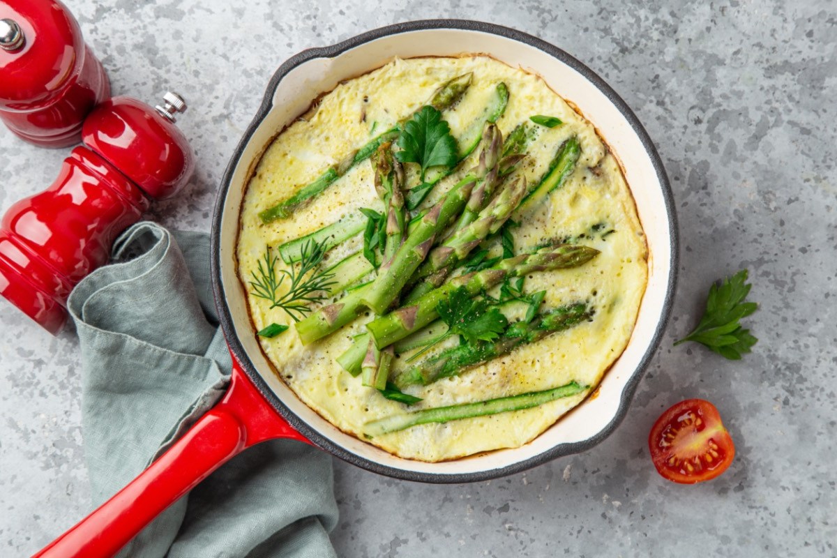 Ein Spargel-Omelett in einer roten Pfanne in der Draufsicht. Daneben liegen Pfeffer- und Salzmühlen in Rot.