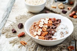 Süße Quinoa-Bowl in weißer Schüssel, garniert mit Haselnüssen, Pekannüssen, Kokosraspeln und Schokolade.