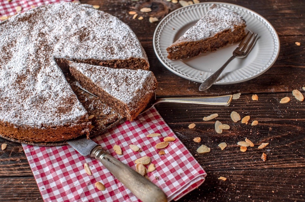 Torta Caprese, italienischer Schoko-Mandel-Kuchen, auf einem weißen Teller. Daneben ein Teller mit einem Stück Kuchen.