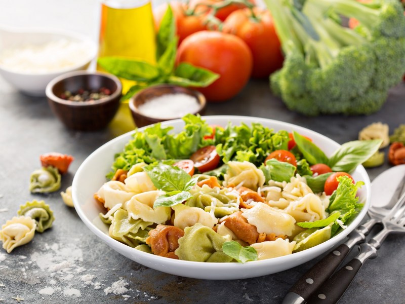 Tortellini-Salat mit Tomaten und Basilikum auf einem Teller.