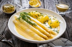 ein Teller weißer Spargel mit veganer Sauce hollandaise und Kartoffeln und Petersilie, daneben je eine Schale mit Butter, mit Zitronen und Soße.