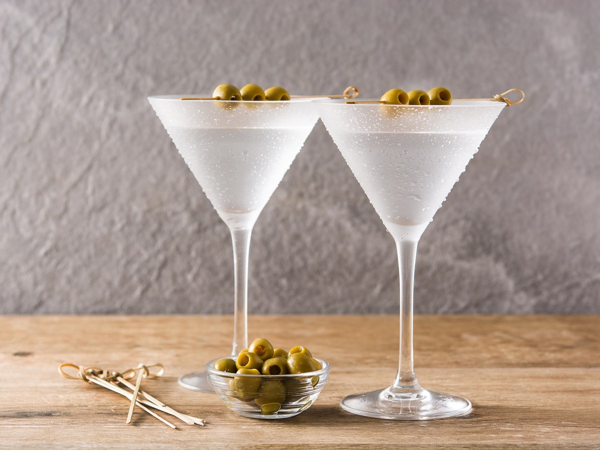 Zwei Gläser dry Martini auf einem Holztisch, garniert mit Oliven.