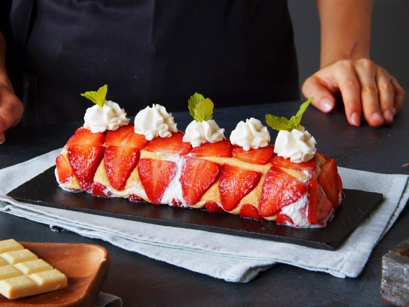 Einfache Erdbeer-Biskuitrolle dekoriert mit Sahnetupfen.