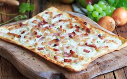 Ein Elsässer Flammkuchen auf einem Holzbrett.