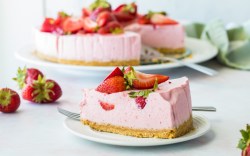 Ein Stück Erdbeer-Käsekuchen auf einem Teller. Im Hintergrund ist der restliche Kuchen zu sehen.