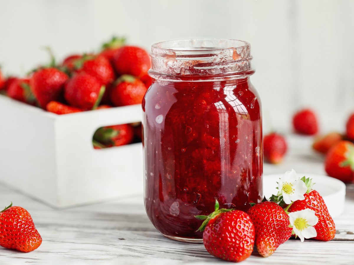 Erdbeermarmelade selber machen: Ein Glas Erdbeermarmelade, daneben und dahinterliegen frische Erdbeeren.