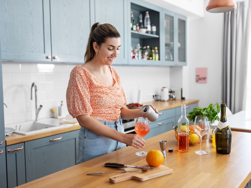 Hausbar-Ausstattung: Eine Frau macht einen Orangen-Cocktail in ihrer Küche